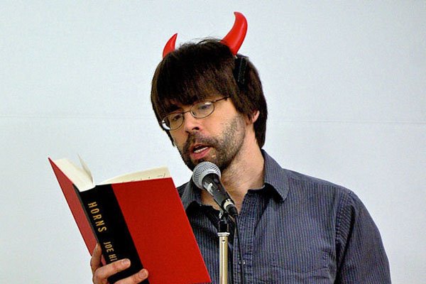 Joe Hill (autor) lendo seu livro vestindo chifres de plástico na cabeça